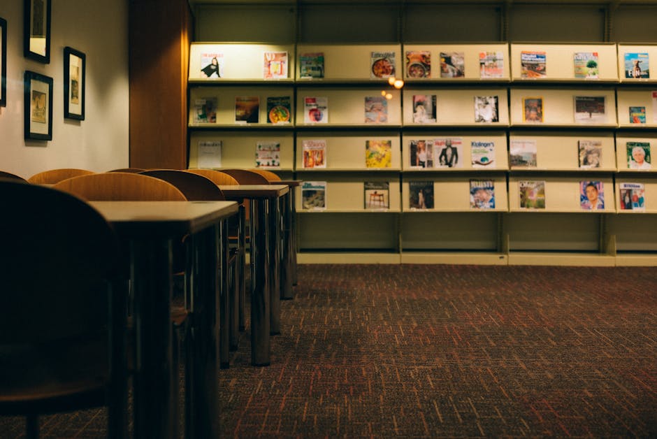 A quiet library setting featuring empty wooden chairs and various magazines displayed on shelves.