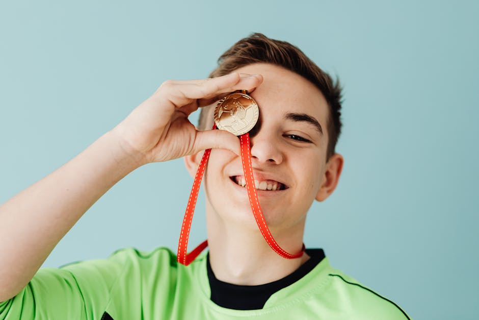 Teenager celebrating a soccer win with a gold medal, smiling joyfully in a bright studio portrait.