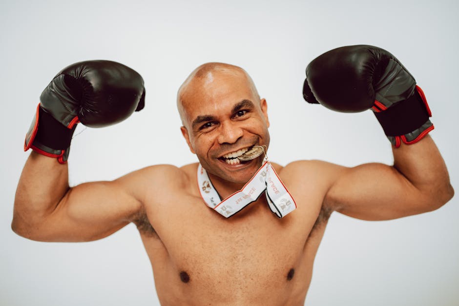 A victorious boxer poses confidently with boxing gloves and a medal in a studio setting.